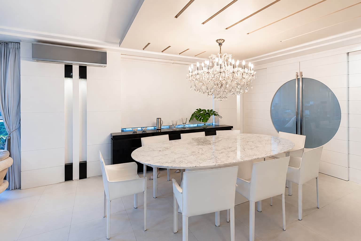 Sala de jantar clara com mesa oval de mármore e lustre de cristal