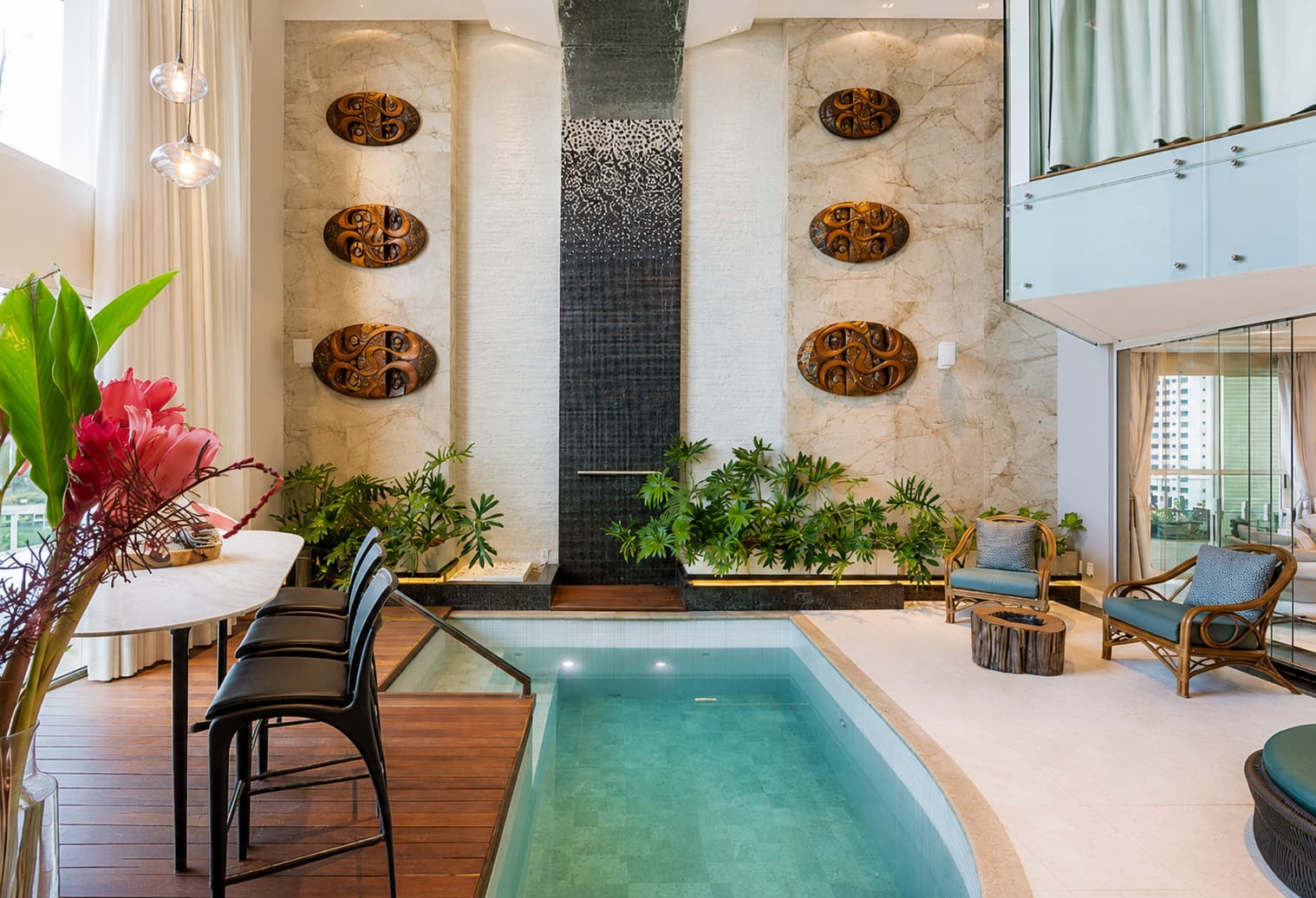 Piscina interna com parede monumental, vegetação e mobiliário