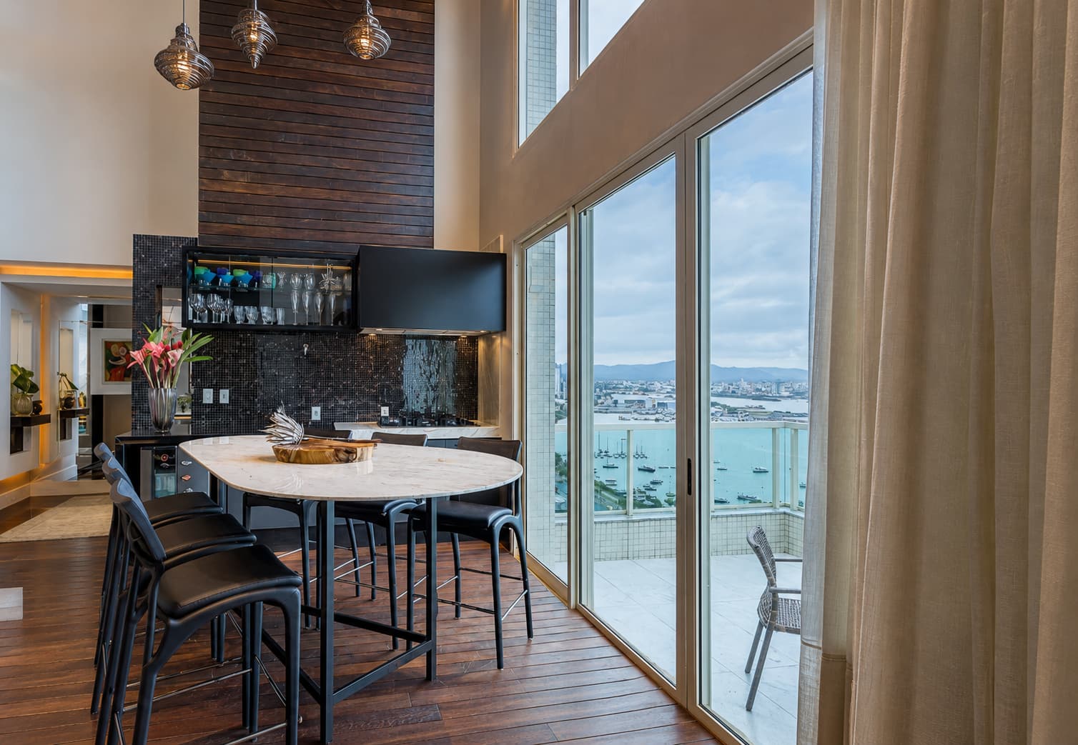 Área gourmet com mesa alta, grandes esquadrias e vista para a água